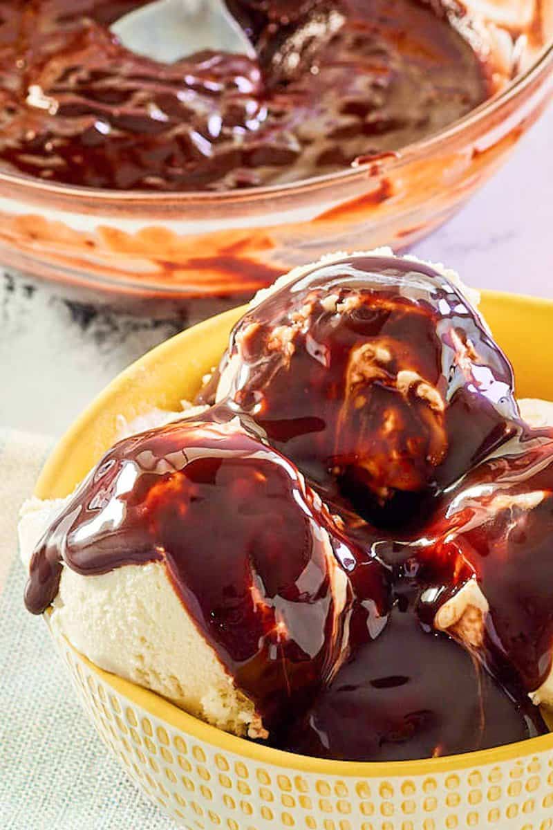 Closeup of homemade hot fudge sauce on top of vanilla ice cream and in a bowl.