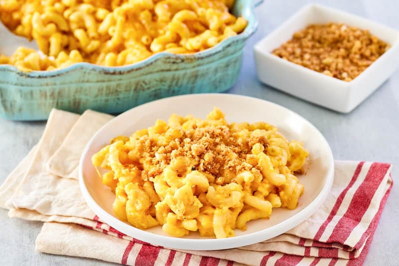 Mac and cheese with bread crumbs serving on a plate in front of the dish.