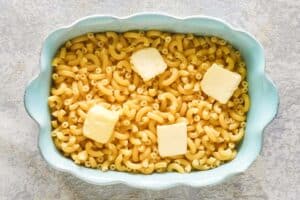 Cooked macaroni and butter pieces in a baking dish.