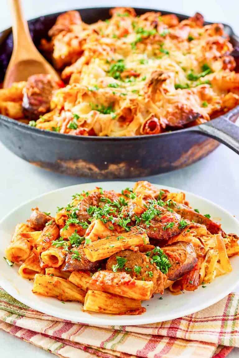 One pot sausage pasta in a skillet and a serving of it on a plate.