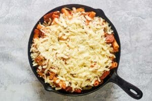 Italian sausage pasta with shredded mozzarella on top before broiling.