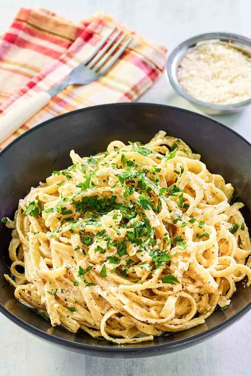 Copycat Pasta House fettuccine alfredo in a large bowl and parmesan cheese in a small bowl.