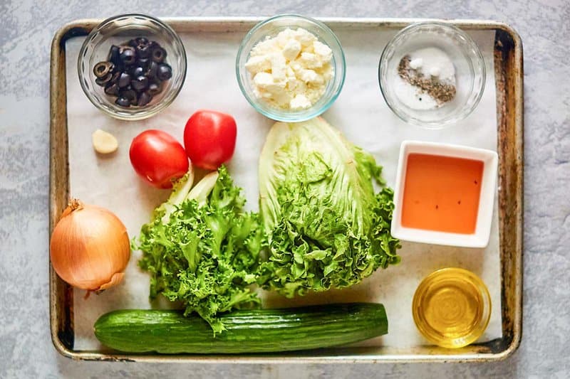 Traditional Greek salad and dressing ingredients on a tray.