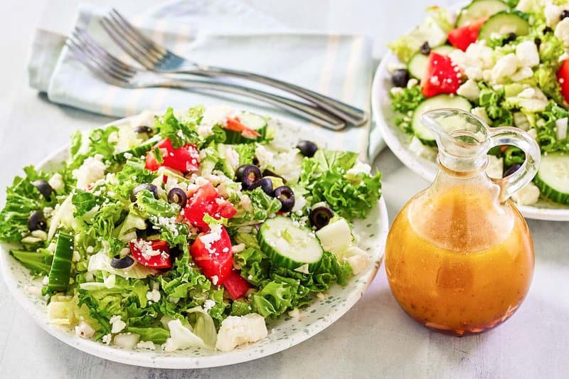 Traditional Greek salad on large salad plates and the dressing in a small pitcher.