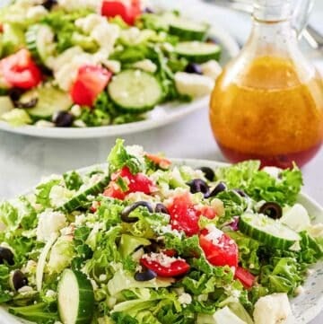 Traditional Greek salad on two plates and the dressing in a small pitcher.