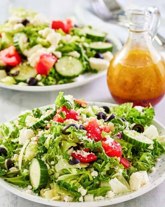 Traditional Greek salad on two plates and the dressing in a small pitcher.