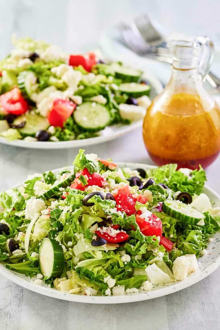 Traditional Greek salad on two plates and the dressing in a small pitcher.