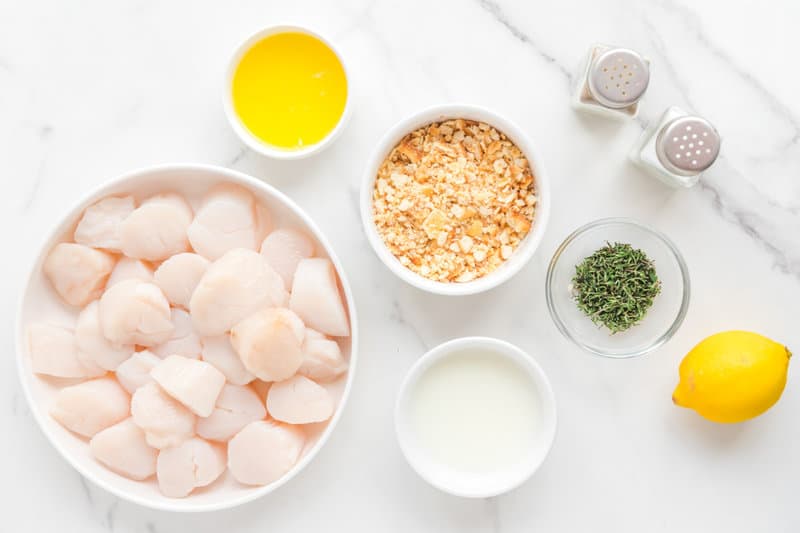 Ingredients for baked scallops with Ritz crackers on a marble surface.