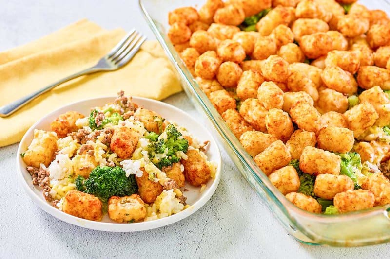 Broccoli tater tot casserole serving on a plate next to the casserole.