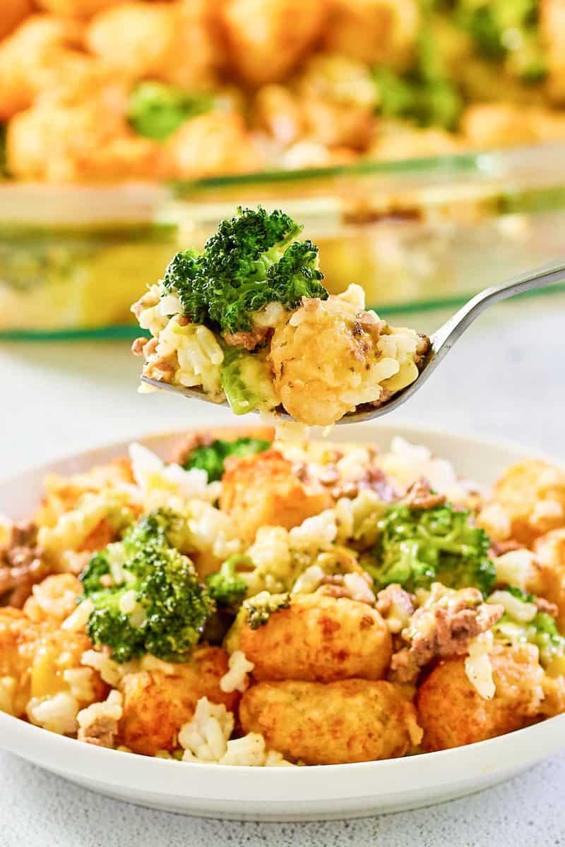 Broccoli tater tot casserole with ground beef on a fork over a plate of it.