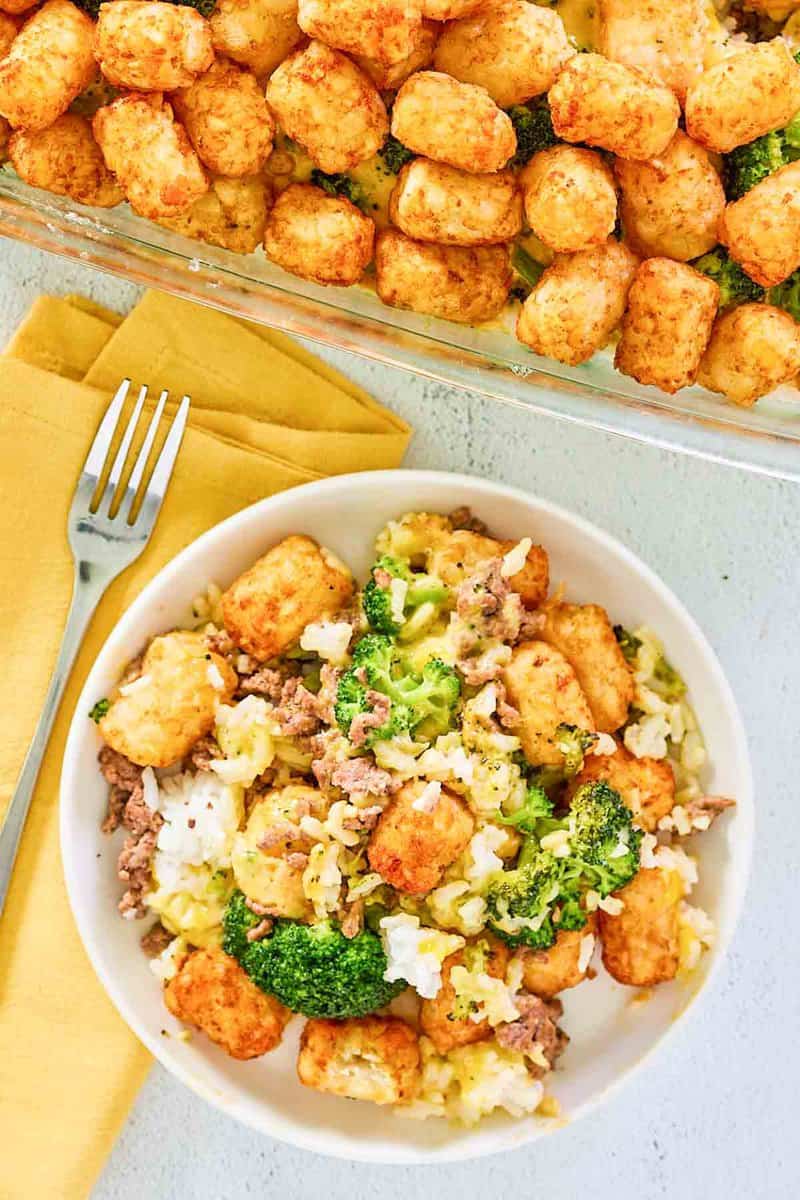 Overhead view of broccoli tater tot casserole with beef in a baking dish and a bowl.