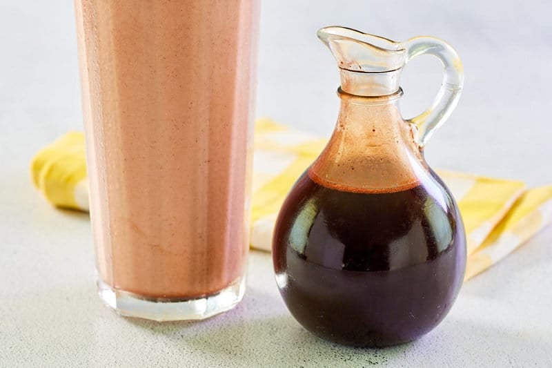 Homemade chocolate syrup next to a glass of chocolate milk.