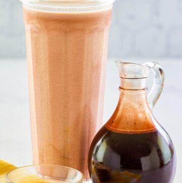 Homemade chocolate syrup in a small glass pitcher and a glass of chocolate milk.