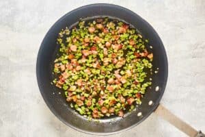 Cooked diced bacon and vegetables in a skillet.