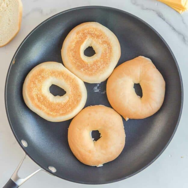 Toasting buttered bagels in a skillet.