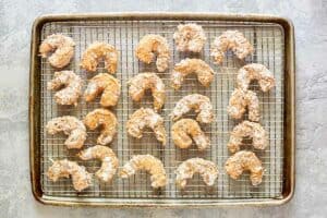 Battered shrimp on a wire rack over a baking sheet.