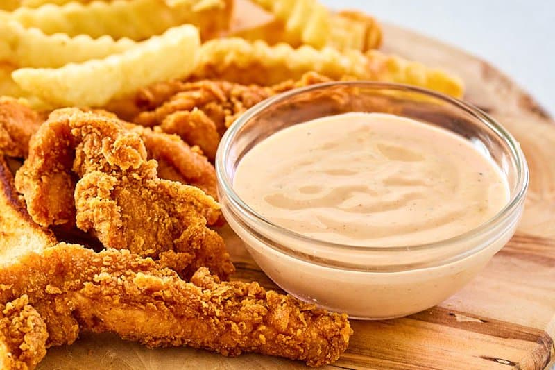 A bowl of copycat Zaxby's zax sauce, fried chicken fingers, and crinkle fries.