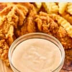 Homemade Zaxby's Zax sauce in a small glass bowl, fried chicken tenders, and crinkle fries.