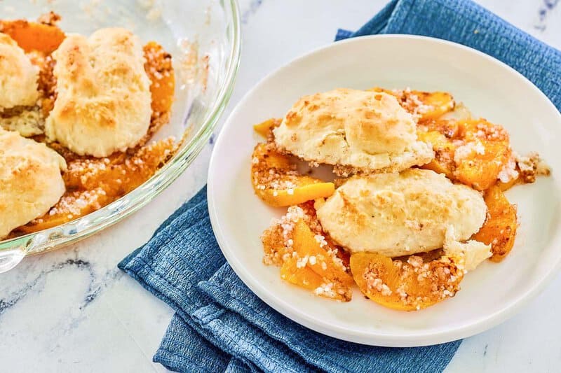 Bisquick peach cobbler on a plate and in a glass pie dish.