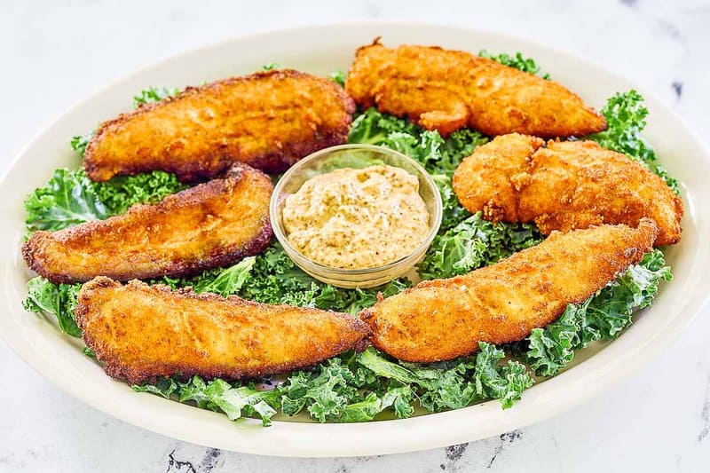 Copycat Planet Hollywood Captain Crunch chicken tenders and a bowl of Creole mustard on a white platter.