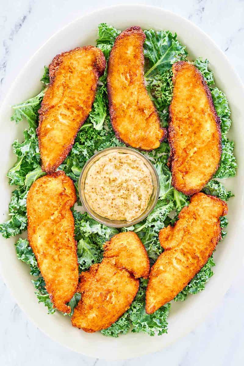 Overhead view of copycat Planet Hollywood Captain Crunch chicken tenders and a bowl of Creole mustard on a platter.