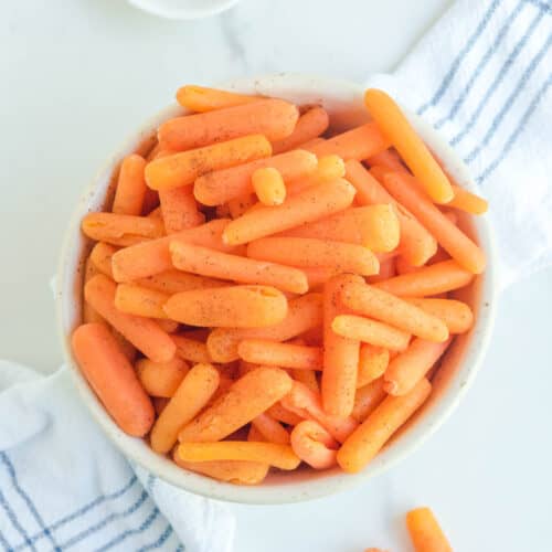 Overhead view of copycat Cracker Barrel baby carrots and a small bowl of ground nutmeg.