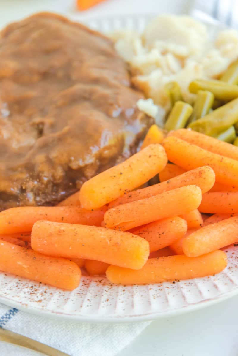 Copycat Cracker Barrel baby carrots on a plate with chopped steak, green beans, and mashed potatoes.