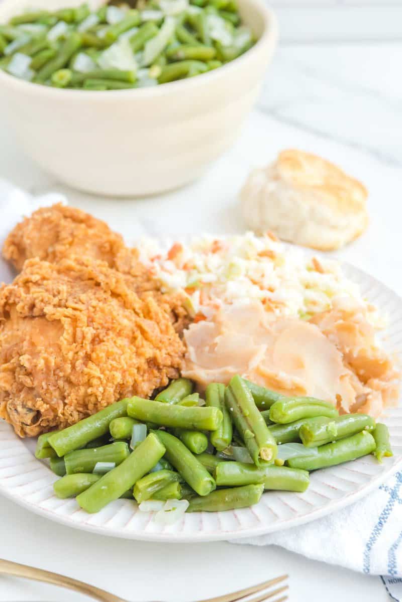 Copycat KFC green beans on a plate with fried chicken, mashed potatoes, and cole slaw.