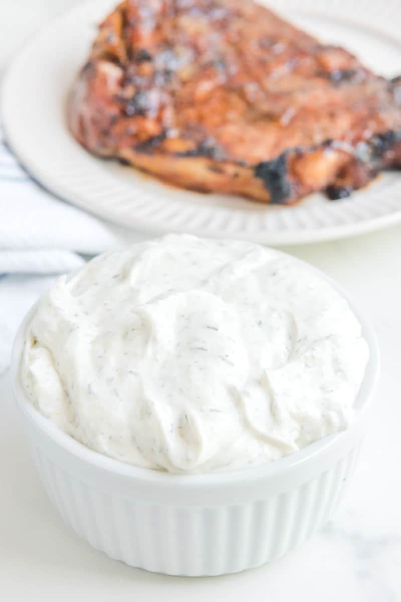 A vessel  of copycat Outback tiger dill condiment  and a steak connected  a plate.