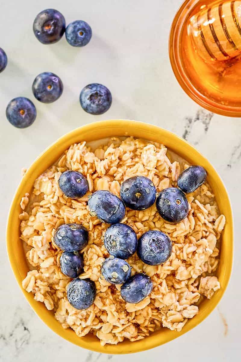 Blick von oben auf Overnight Oats aus Milch, frischen Blaubeeren und einer Schüssel Honig.