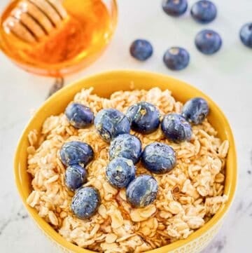 Overnight oats made with milk in a bowl, fresh blueberries, and a bowl of honey.