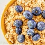 Closeup of a bowl of overnight oats made with milk and topped with blueberries and honey.