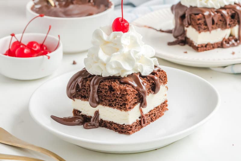 Copycat Shoney's hot fudge cake on a plate and a bowl of maraschino cherries.