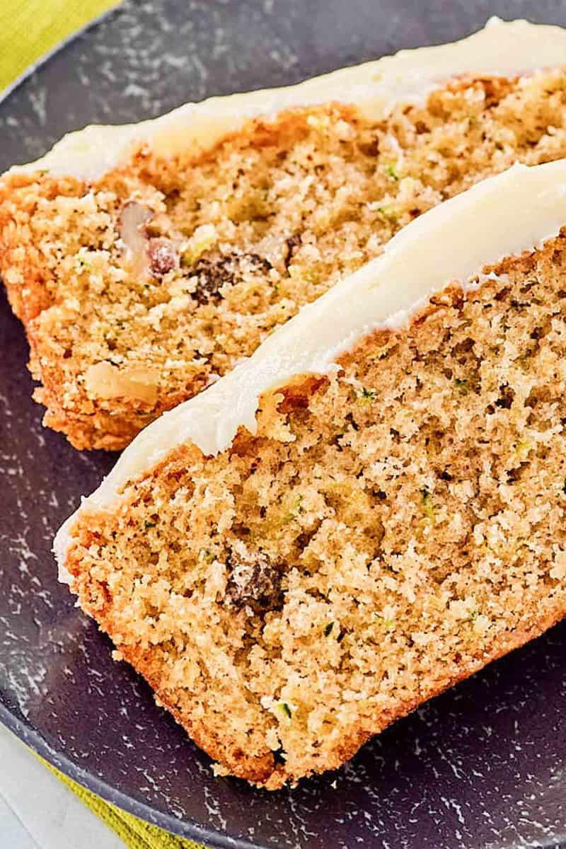 Closeup of two slices of zucchini nut bread with cream cheese frosting.