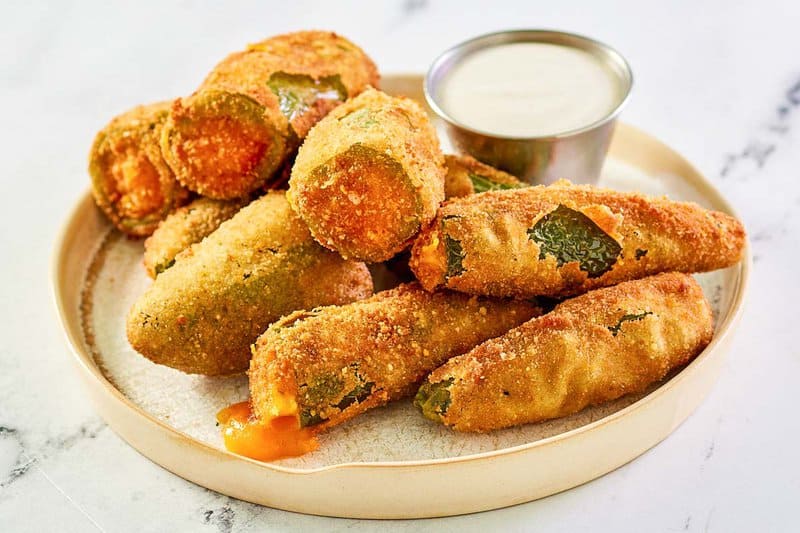 Deep fried cheddar cheese jalapeno poppers and dipping sauce on a plate.