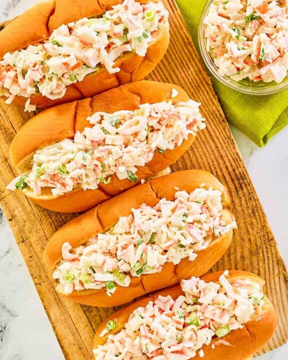 Overhead view of imitation crab salad in hoagie rolls and a small glass bowl.