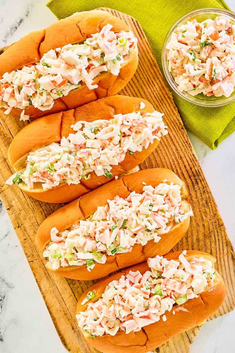 Overhead view of imitation crab salad in hoagie rolls and a small glass bowl.