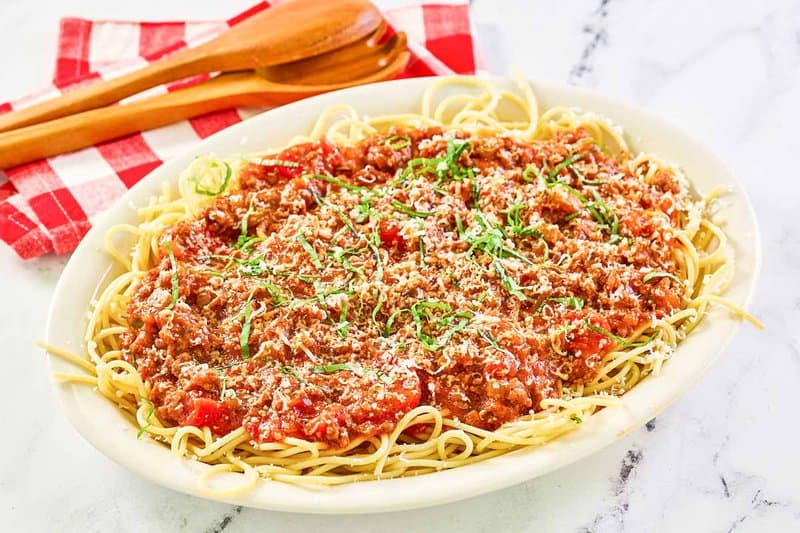 Homemade meat sauce over spaghetti pasta on a white platter.