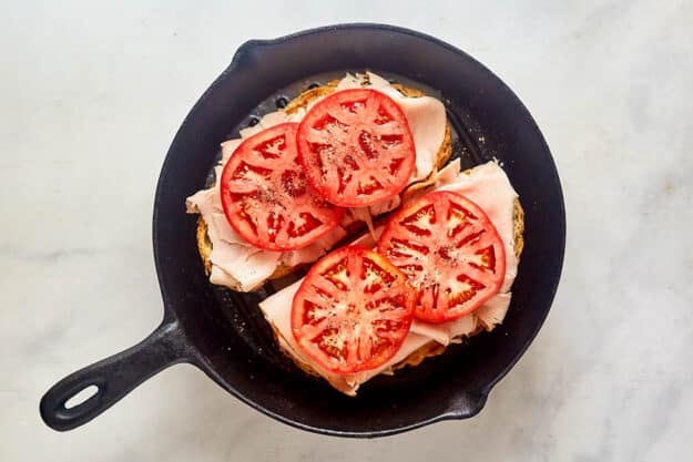 Toasted bread, turkey slices, and tomato slices in a skillet.