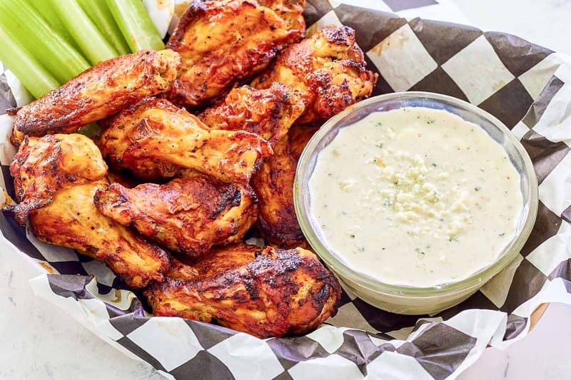 Copycat Wingstop blue cheese dip, chicken wings, and celery in a parchment paper lined basket.