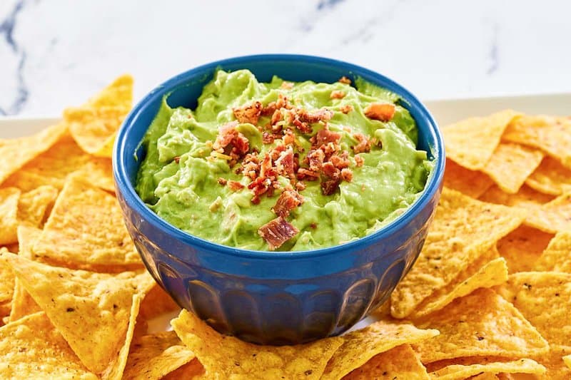 A bowl of avocado dip and tortilla chips on a white platter.