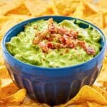 A bowl of avocado dip and tortilla chips on a platter.