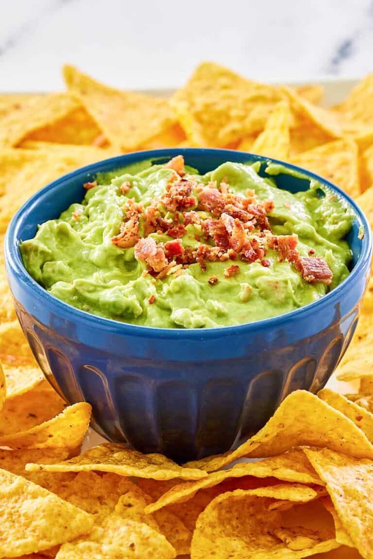 A bowl of avocado dip and tortilla chips on a platter.