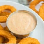 Homemade Burger King zesty sauce in a small metal condiment cup next to onion rings.