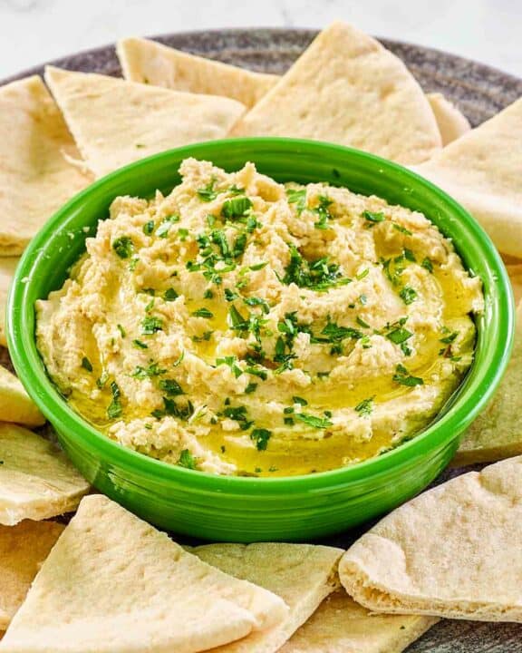 Creamy hummus with yogurt in a green bowl surrounded with pita bread slices.