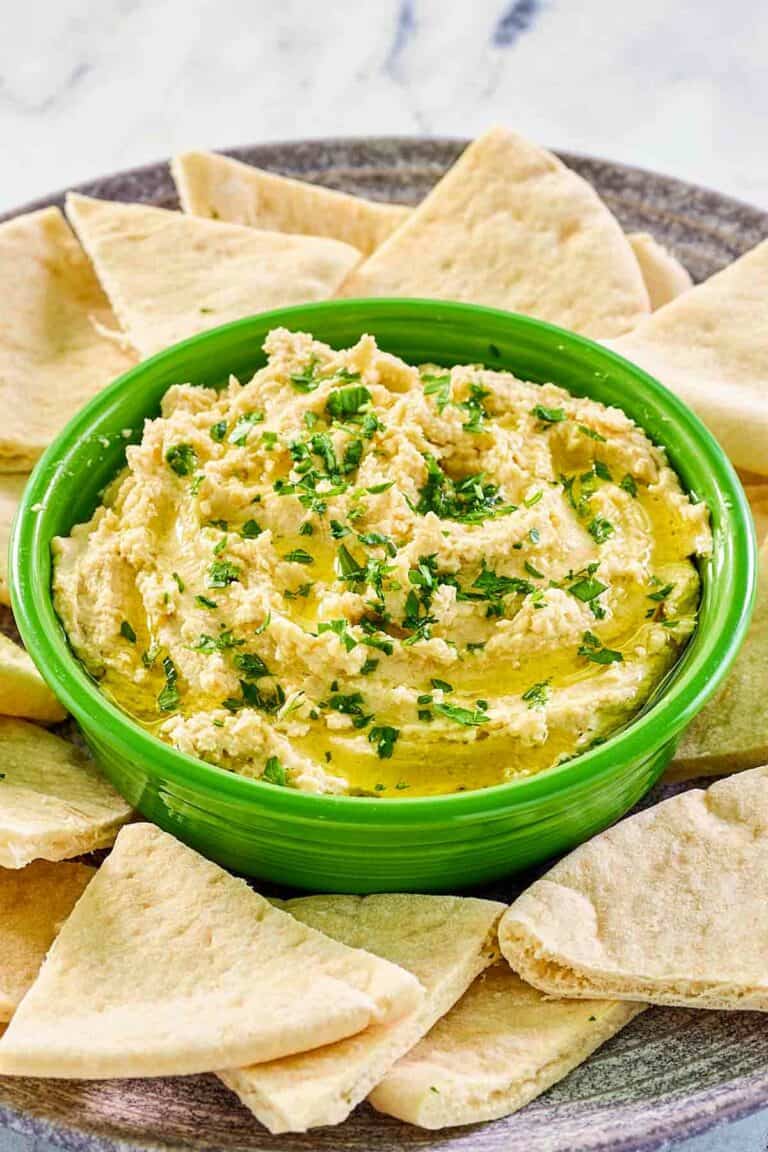 Creamy hummus with yogurt in a green bowl surrounded with pita bread slices.