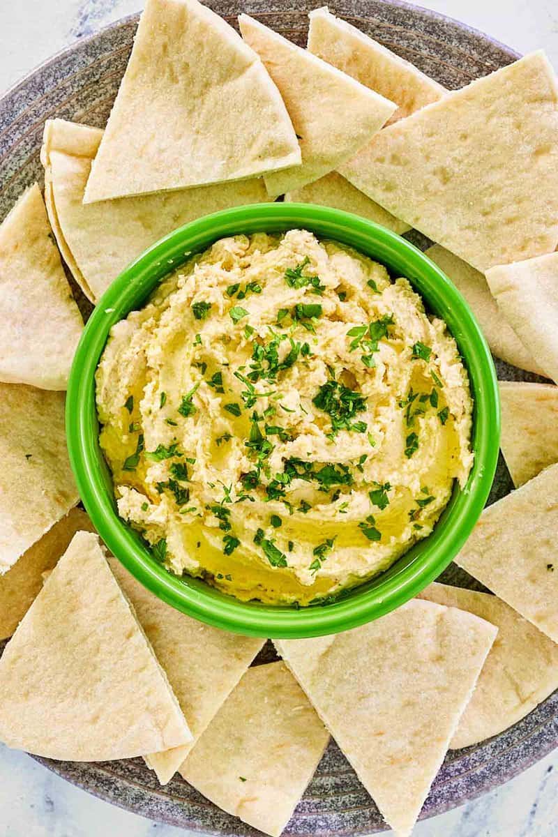 Overhead view of creamy hummus with yogurt and pita bread slices on a platter.