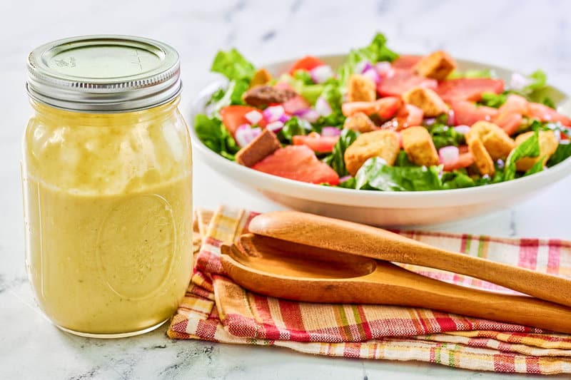 A jar of homemade greenish  bulb  crockery   dressing and a salad.