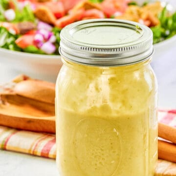 Green onion salad dressing in a mason jar and a salad behind it.