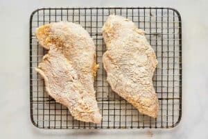 Breaded chicken breasts on a wire rack.